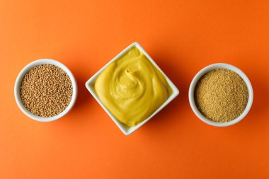 Turuncu arka planda hardal tohumu, sos ve toz dolu kaseler.