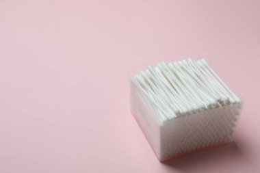 Pembe arka planda pamuk çubukları olan plastik kutu.