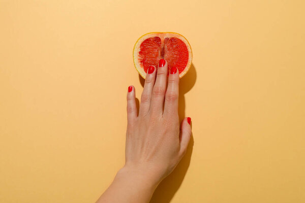 Female hand and grapefruit on beige background