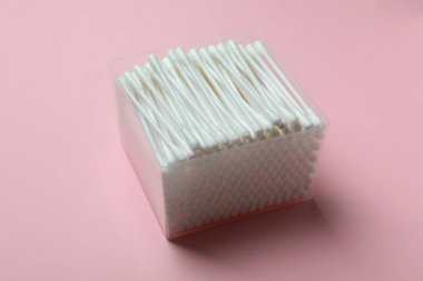 Pembe arka planda pamuk çubukları olan plastik kutu.