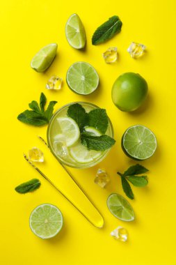 Bir bardak mojito kokteyli ve sarı arka planda malzemeler.