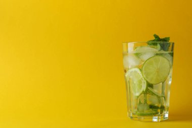 Sarı arka planda bir bardak mojito kokteyli
