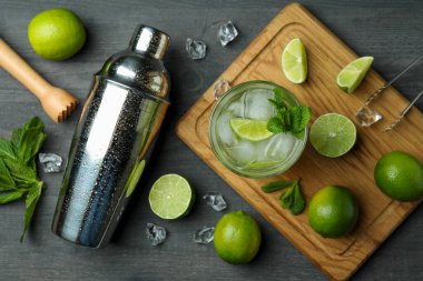 Bir bardak mojito kokteyli, koyu ahşap arka planda malzemeler ve titretici.