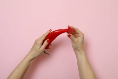 Kadın eli pembe arka planda biber ve prezervatif tutuyor.