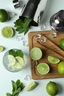 Bir bardak taze mojito kokteyli ve beyaz arka planda malzemeler.