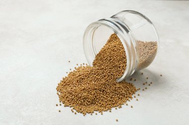 Beyaz desenli arkaplanda hardal tohumları olan cam kavanoz.