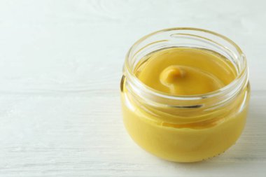 Beyaz ahşap masadaki hardallı cam kavanoz.