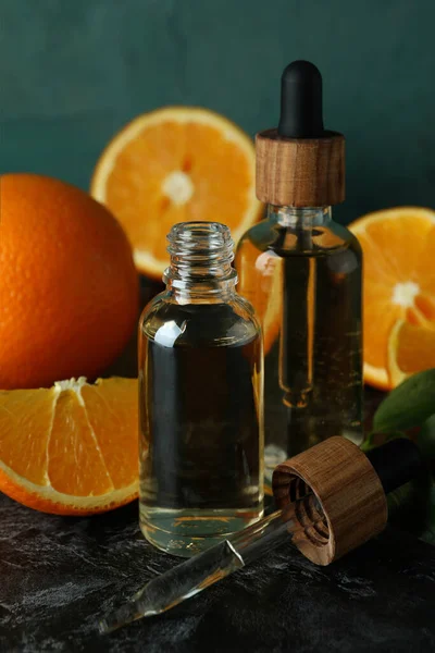 Dropper bottles with oil and oranges on black smoky table