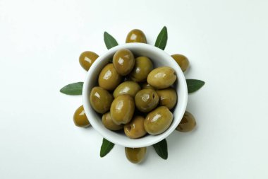 Bir kase yeşil zeytin ve beyaz arkaplanda yapraklar