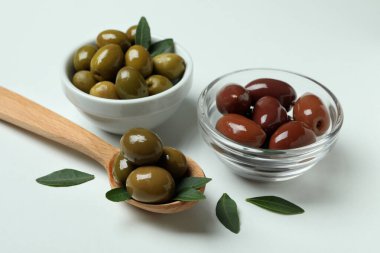 Kâselerle kaşık dolusu zeytin ve beyaz arka planda yapraklar