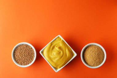 Turuncu arka planda hardal tohumu, sos ve toz dolu kaseler.