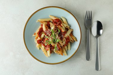 Domates soslu makarna ve beyaz desenli arka planda malzemeler.