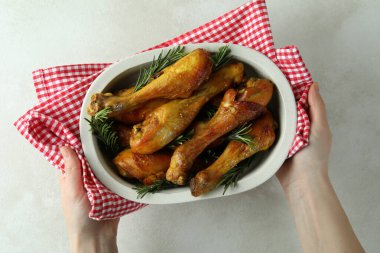 Kadın elleri tavuk budu ile fırın tepsisini tutuyor.