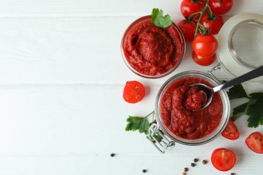 Beyaz ahşap zemin üzerinde domates ezmeli kase ve kavanoz.
