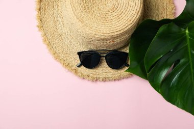 Hasır şapka, palmiye yaprakları ve pembe arka planda güneş gözlüğü.