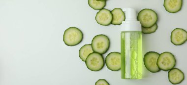 Beyaz arka planda kozmetik ve salatalık dilimleri olan bir şişe.