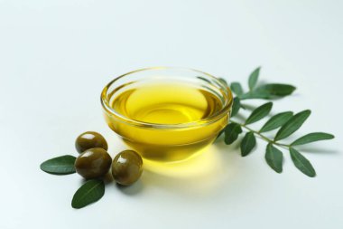 Beyaz arka planda bir kase yağ, zeytin ve dal.