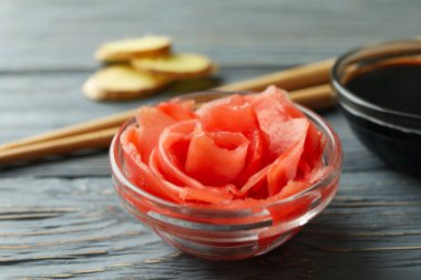 Bir kase turşulu zencefil, soya sosu ve ahşap masada çubuklar.
