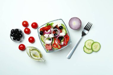 Beyaz arka planda bir kase Yunan salatası ve malzemeleri