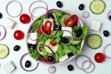 Beyaz arka planda bir kase Yunan salatası ve malzemesi.