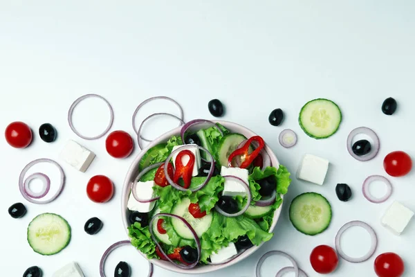 Beyaz arka planda bir kase Yunan salatası ve malzemesi.