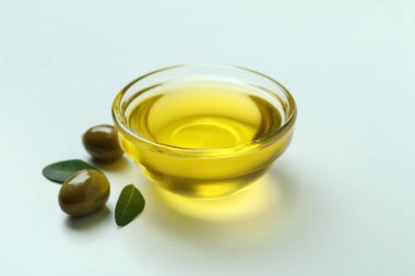 Beyaz arkaplanda bir kase yağ, zeytin ve yapraklar