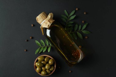 Bir şişe zeytinyağı, bir kase zeytin, dallar ve siyah arka planda biber.