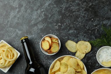 Farklı atıştırmalıklar ve siyah dumanlı arka planda bir şişe bira.