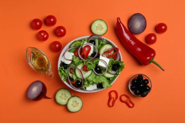 Turuncu arka planda bir kase Yunan salatası ve malzemeleri.