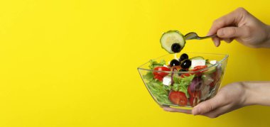 Dişi el çatalı ve sarı arka planda bir kase Yunan salatası.