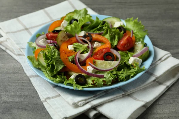 灰色のテクスチャの背景にギリシャのサラダとキッチンタオルのプレート — ストック写真