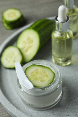 Kozmetik ürünleri ve salatalıklar gri desenli arka planda tepside