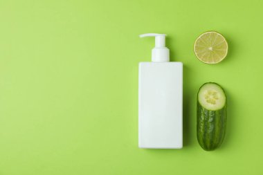 Yeşil arka planda bir şişe kozmetik, salatalık ve limon.