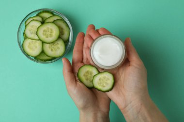 Kadın eli, nane arkaplanında kozmetik ürünleri bulunan salatalık dilimli kavanozu tutuyor.