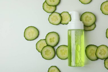 Beyaz arka planda kozmetik ve salatalık dilimleri olan bir şişe.