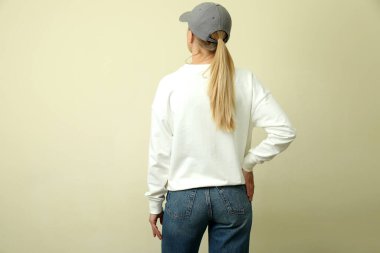 Tişörtlü ve kepli bej arka planda genç bir kadın.