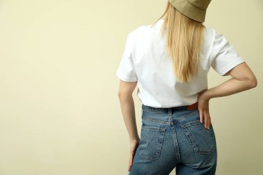 Bej arka planda, tişörtlü ve şapkalı genç bir kadın.