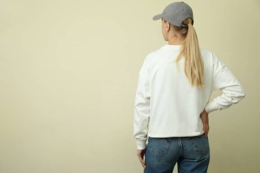 Tişörtlü ve kepli bej arka planda genç bir kadın.