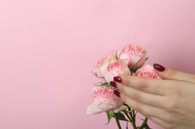 Manikürlü kadın eli ve pembe arka planda güller.