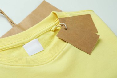 Beyaz arkaplanda etiketli ve çantalı bir kazak