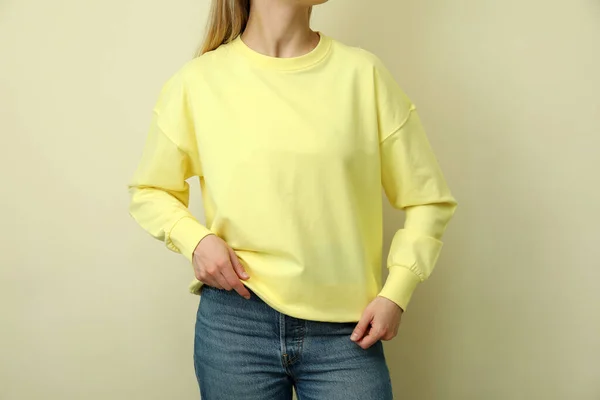 Young woman in yellow sweatshirt against beige background