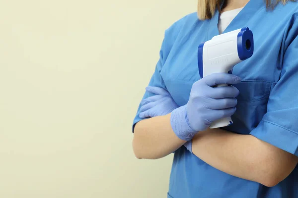 Female doctor hold thermometer gun on beige background