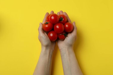 Kadın elleri sarı arka planda kiraz domatesi tutuyor.