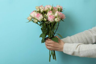 Kadın elleri mavi arka planda gülleri tutar