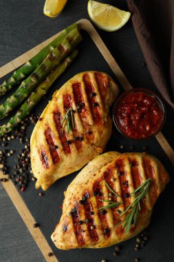 Koyu ahşap arka planda ızgara tavuk ve malzemeli pano.