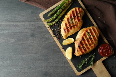 Koyu ahşap arka planda ızgara tavuk ve malzemeli pano.