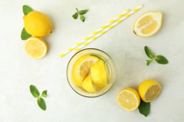 Beyaz desenli masada bir bardak limonata, pipet ve limon.