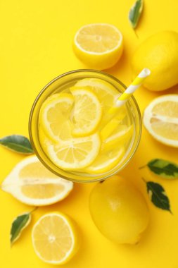 Sarı arka planda bir bardak limonata ve limon.