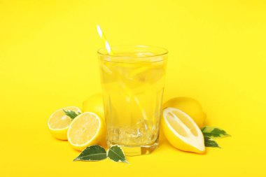 Sarı arka planda bir bardak limonata ve limon.