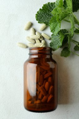 Beyaz desenli arka planda bitkisel haplarla dolu bir şişe.